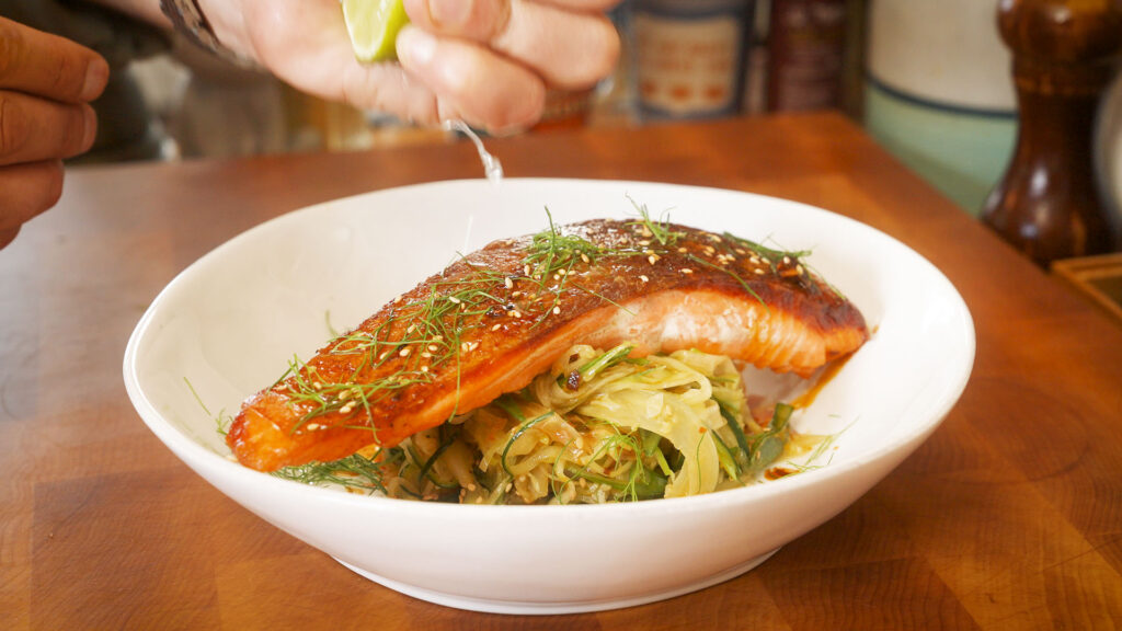 a bowl containing a pan seared salmon fillet over a spicy veggie salad