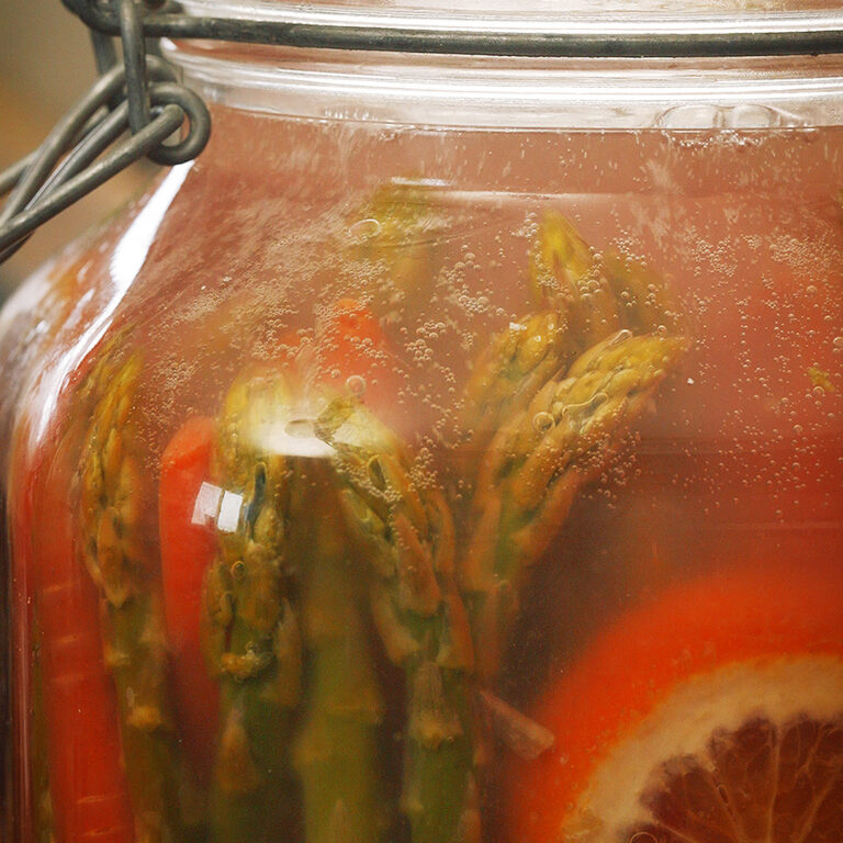 a bubbling jar full of fermented asparagus, carrots and citrus