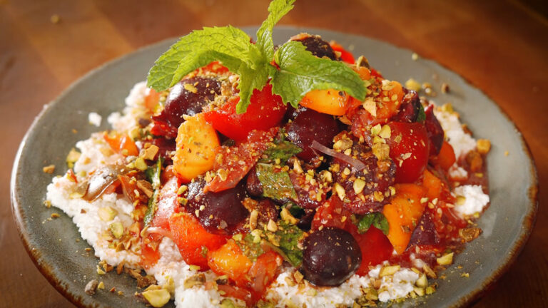 a plate full of a salad made of stone fruit, tomatoes, pistachios and ricotta cheese.
