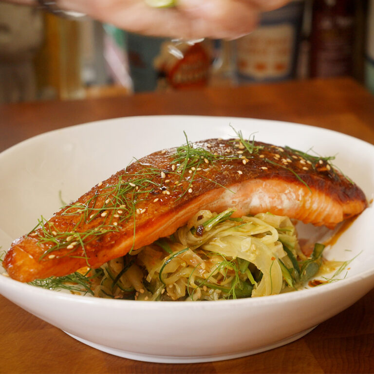 a bowl containing a pan seared salmon fillet over a spicy veggie salad