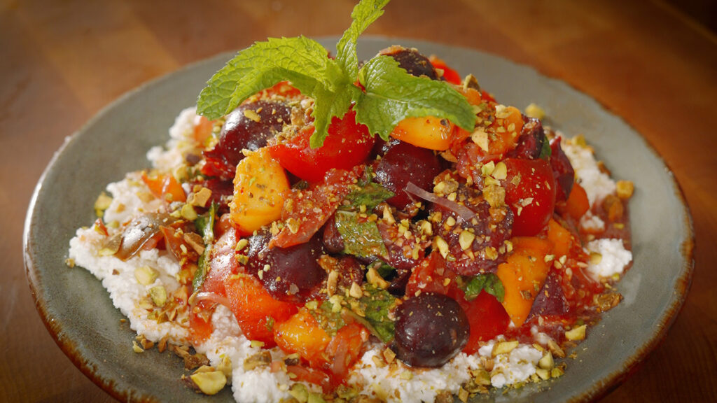 a plate full of a salad made of stone fruit, tomatoes, pistachios and ricotta cheese.
