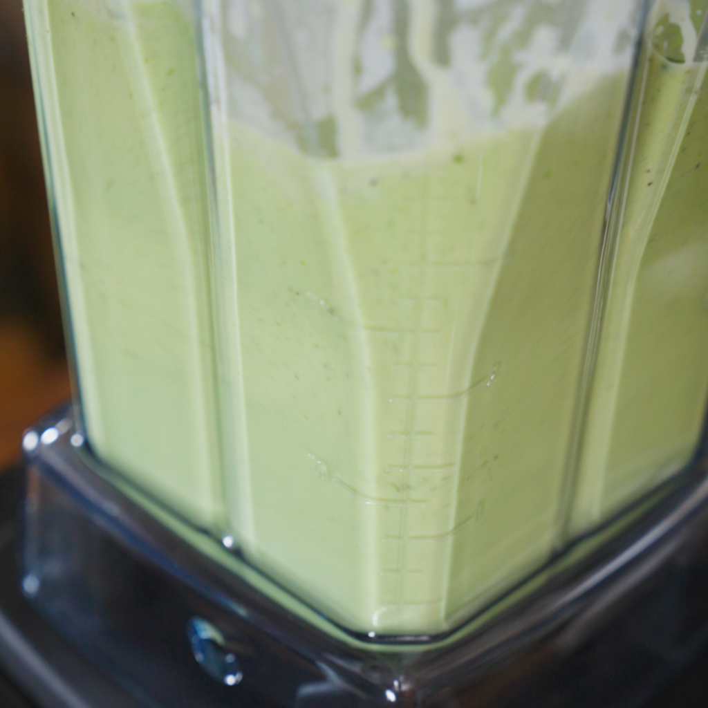 A blender filled with a smooth, pale green sauce blending until fully creamy and uniform.
