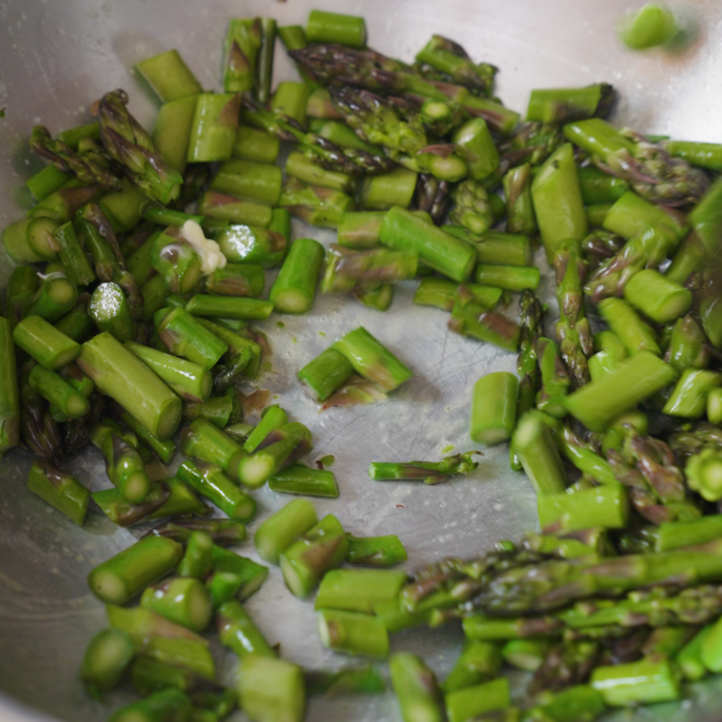 Asparagus pieces cook in a pan, turning bright green and glossy as they sauté in butter.