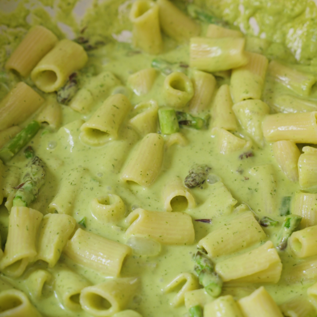 Rigatoni pasta is coated in a glossy green sauce with asparagus pieces, creating a creamy, fully combined dish.